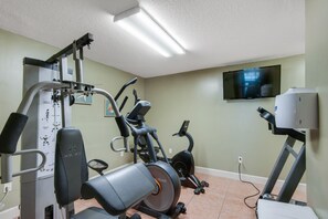 Un gimnasio en casa con una máquina de press de banca, una elíptica, una bicicleta estática y una cinta de correr.