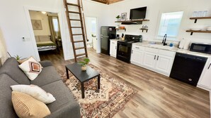 A modern apartment with a loft bedroom, a kitchen with white cabinets, a dining area, and a living room with a gray sofa and a coffee table. - Bass Cabin: Arcade, Inflatables, Fishing & More! (Guntersville)