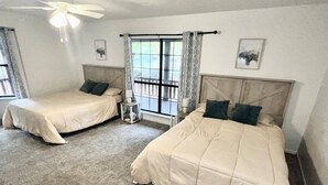 A hotel room with two beds, a ceiling fan, a window with curtains, and a small table.