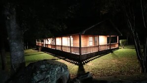 A wooden cabin with a deck, surrounded by trees and a well-maintained lawn.