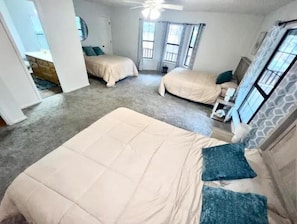 Une chambre avec deux lits, un ventilateur de plafond et une vue sur l’extérieur grâce à de grandes fenêtres.