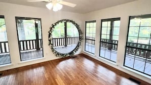 A spacious room with large windows, a wooden floor, and a ceiling fan.