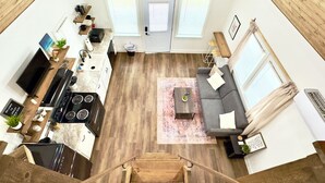 Eine moderne Küche mit Herd, Spüle und Essbereich. Ein Wohnzimmer mit Sofa und Fernseher ist ebenfalls vorhanden. Der Raum verfügt über Holzböden und einen Deckenventilator.