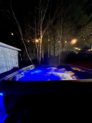Ein Whirlpool mit blauer Beleuchtung, umgeben von Bäumen und Lichterketten.