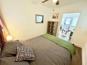 Ein Schlafzimmer mit einem Bett, einer Nachttischlampe, einem Spiegel und einer Tür zu einem Wohnbereich.