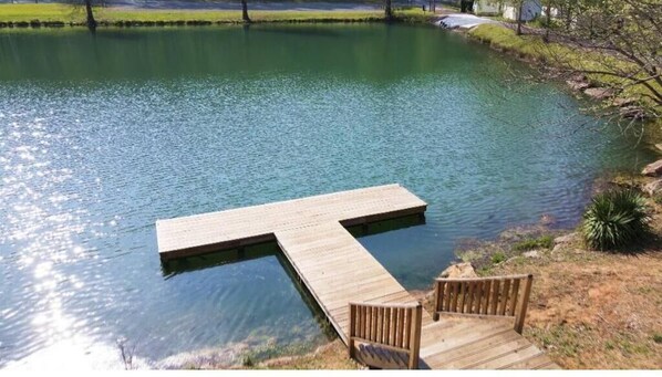A wooden dock extending into a calm body of water, with a bench and a chair on the dock.