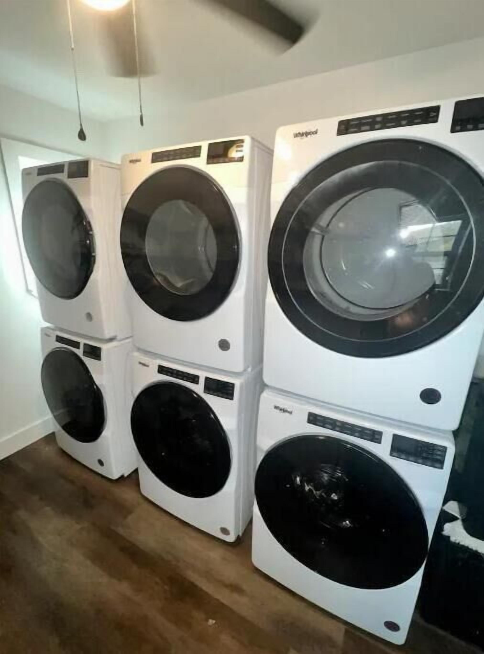 A stack of four front-loading washing machines in a room with wooden flooring and a white ceiling.