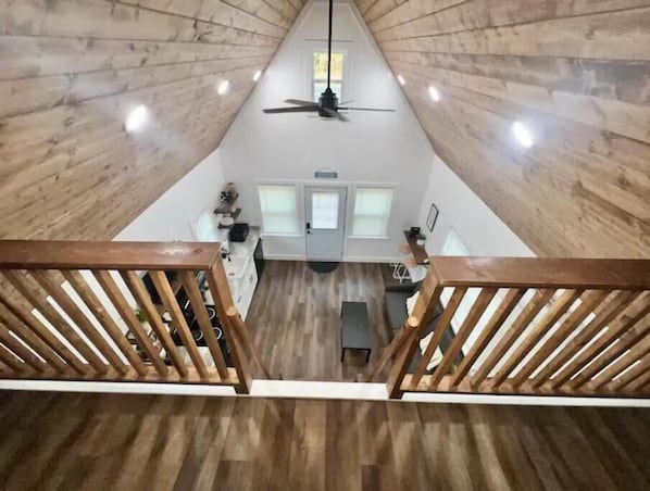 A high-ceilinged room with wooden walls and a central ceiling fan.