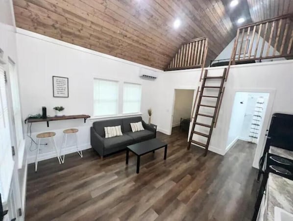 A spacious living area with a wooden ceiling, a sofa, a coffee table, and a staircase leading to an upper level.