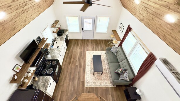 A spacious loft with a high ceiling, wooden beams, a kitchen with modern appliances, a seating area with a sofa and rug, and large windows providing natural light. - Raccoon Cabin: Arcade, Kayaks, Inflatables, & More (Guntersville)