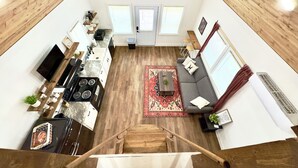 A spacious living area with a kitchen, a dining table, and a sofa. There is a ceiling fan, a staircase, and a window with blinds. - Rabbit Cabin: Arcade, Fishing, Kayaks, & More! (Guntersville)