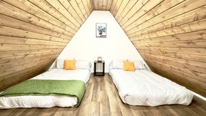 Un dormitorio acogedor en el ático con dos camas, paredes de madera, una mesita y un cuadro en la pared.