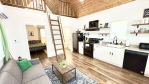 Amplia sala de estar con entrepiso-dormitorio, techo de madera y cocina con alacenas blancas y electrodomésticos modernos.