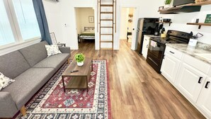 Ein geräumiges Wohnzimmer mit hoher Decke, einer Holztreppe, einer Küche mit modernen Geräten und einer gemütlichen Sitzecke mit Sofa und Couchtisch.