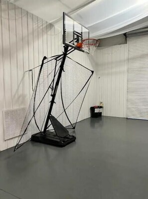 A basketball hoop with a backboard and net, set up in a room with white walls and a grey floor.