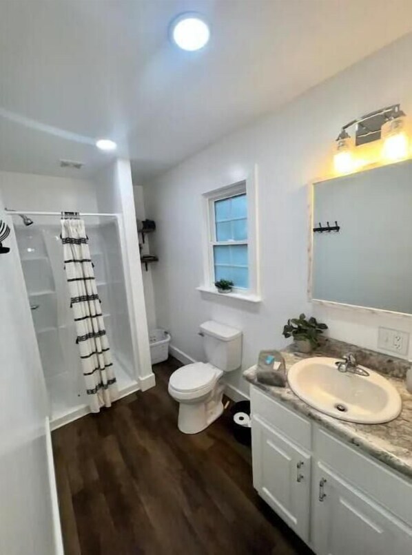 A bathroom with a shower, toilet, sink, and a window.