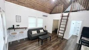 A spacious living area with a wooden ceiling, a sofa, a coffee table, and a staircase leading to an upper level.