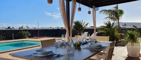 A dining area with a pool view, outdoor seating, and hanging wicker lamps.