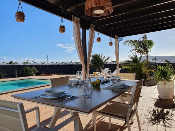 A dining area with a pool view, outdoor seating, and hanging wicker lamps. - Escape to Paradise:Villa Perla Nera – Your Oasis of Comfort and Serenity!
(Playa Blanca)