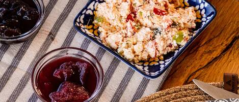 Diversos alimentos, como queso, nueces y un plato con verduras y cereales, sobre un mantel a rayas.