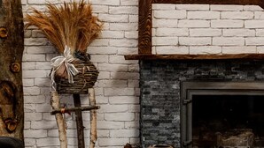 Habitació rústica amb paret de maó blanc, estructura de bigues de fusta, una llar de foc i taula rodona de fusta amb llenya tallada.