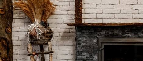 A rustic room with a white brick wall, a wooden beam structure, a fireplace, and a round wooden table with cut wood pieces.