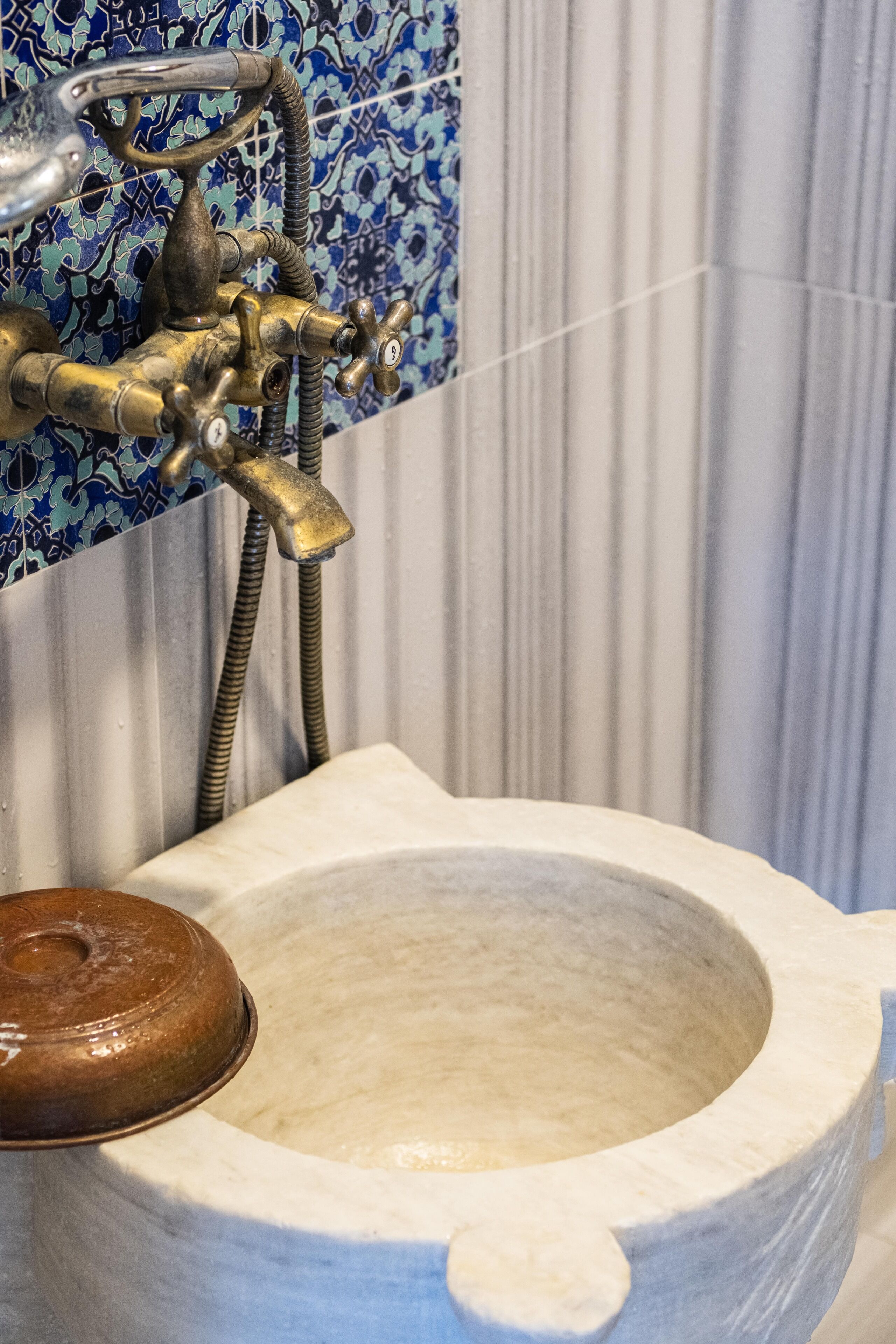 A bathroom with a white ceramic sink, a brass faucet, and a blue patterned tile backsplash.