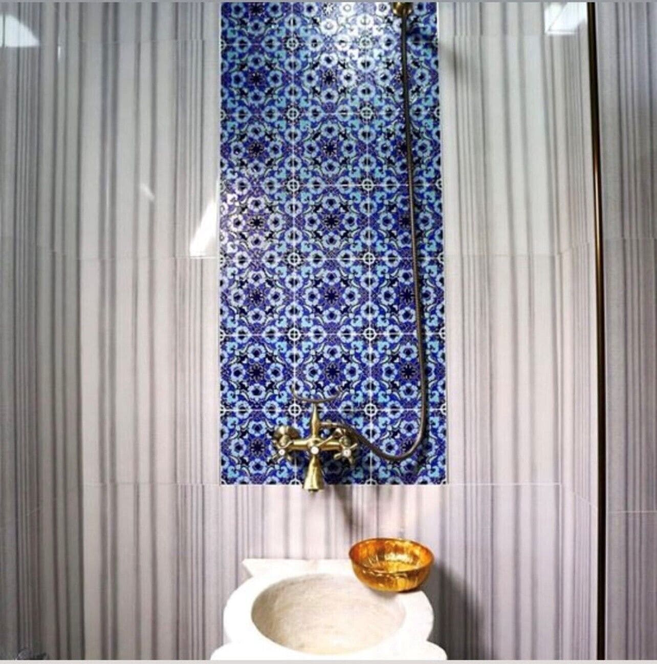 Een badkamer met een blauw betegelde muur, een gouden kraan en een gouden kom op de wastafel.