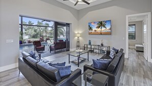 A spacious living room with a large window, a ceiling fan, and a view of a swimming pool and palm trees.