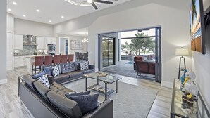 A spacious living area with a sofa, coffee table, and a view of the kitchen and outdoor patio.