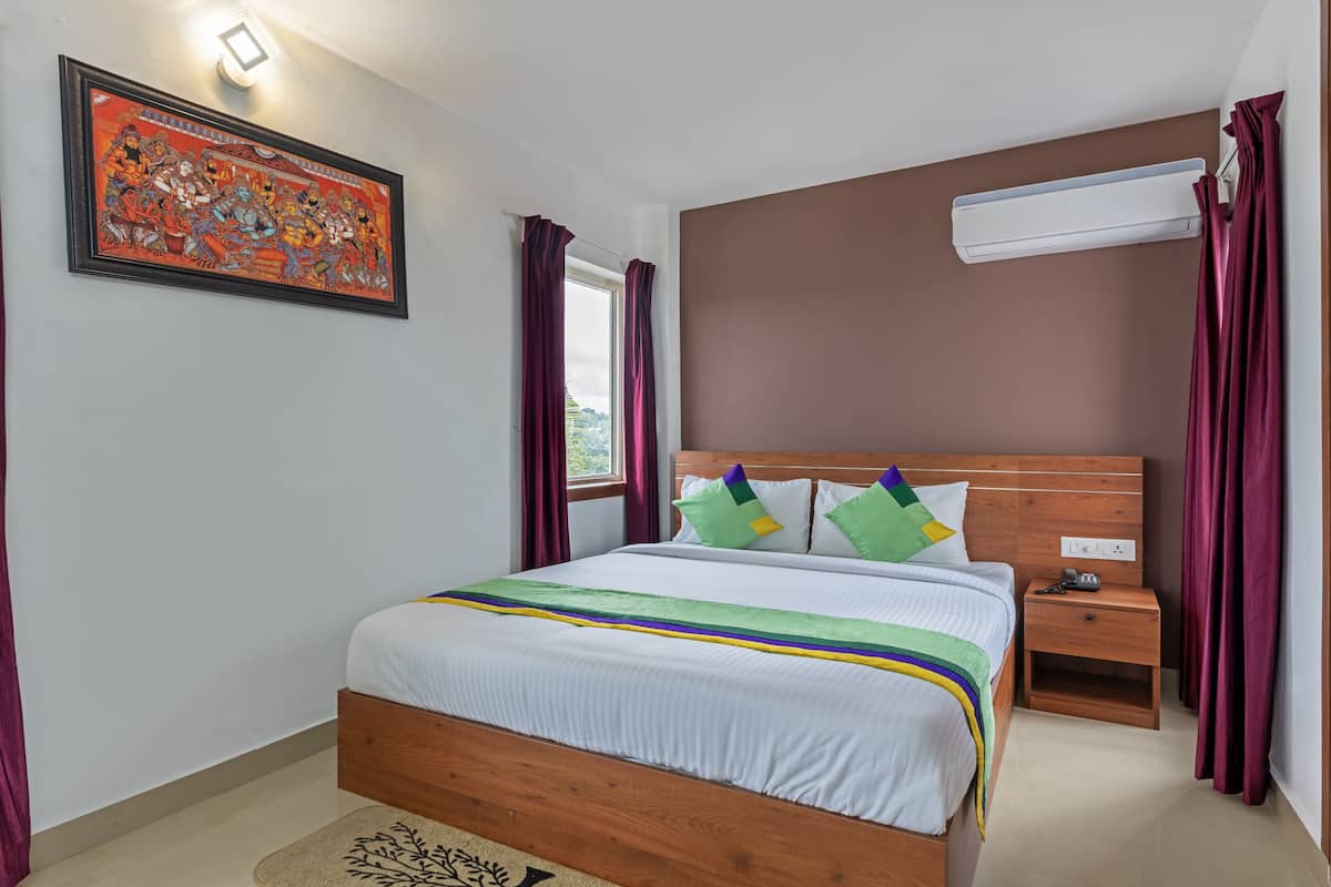 Quarto bem arrumado com cama de madeira, mesa de cabeceira, ar condicionado fixado na parede e um quadro emoldurado sobre a cama.