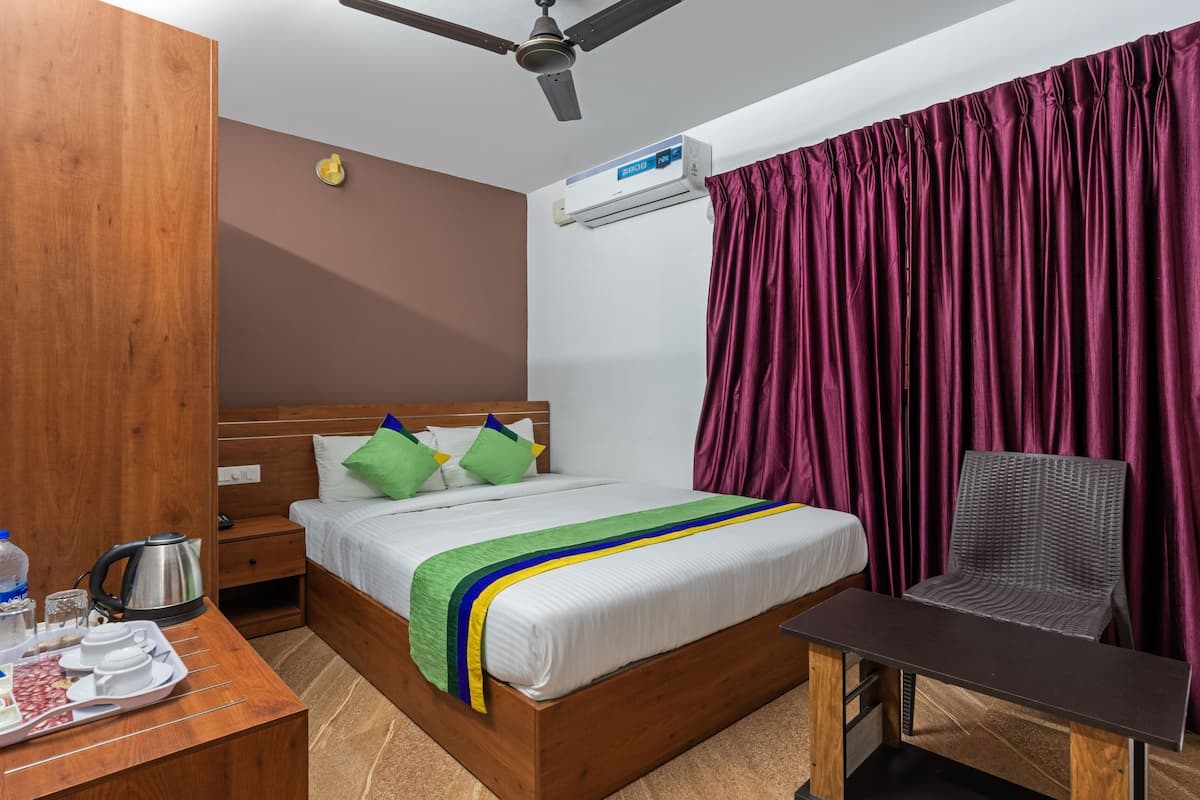 Quarto de hotel com cama de madeira, escrivaninha com itens de café da manhã, uma cadeira e ventoinha no teto.
