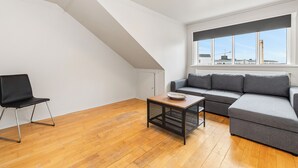 Een modern loft appartement met een schuine plafond, een grijze hoekbank, een zwarte stoel en een houten salontafel.