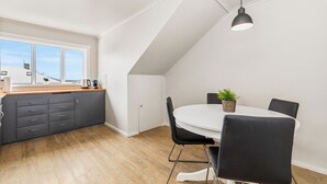 Een moderne keuken met een groot raam, een eethoek met een ronde tafel en stoelen, en een plafondlamp.