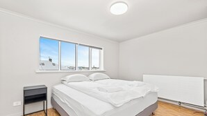 Een moderne slaapkamer met een bed, een nachtkastje, een raam met uitzicht op de stad en een witte radiator.