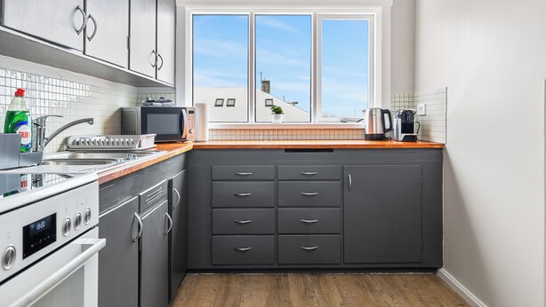 Een moderne keuken met grijze kastjes, een ingebouwde oven en een raam met uitzicht op gebouwen.