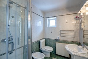Un baño con ducha de vidrio, inodoro, bidé, lavabo y radiador.