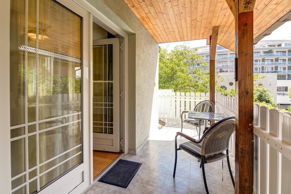 Un balcón con techo de madera, puerta de cristal, una silla y una mesa.