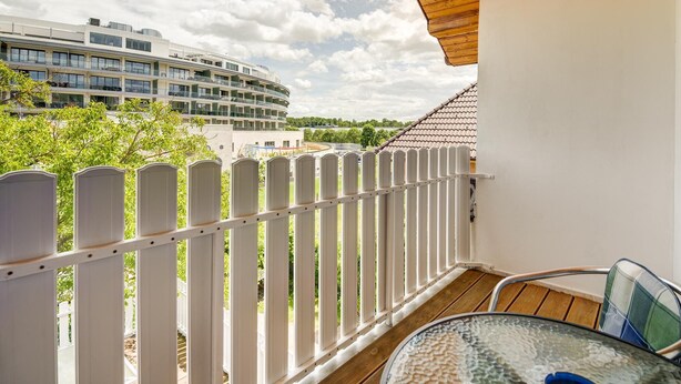 Un balcon doté d’une balustrade blanche, d’une table en verre et offrant une vue sur un immeuble moderne à plusieurs étages.