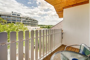 A balcony with a white fence, a glass table, and a view of a modern building with multiple floors. - Studio Apartment in Heviz  3 (Hévíz)