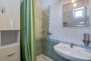 Un baño con ducha, lavabo, espejo y armario.