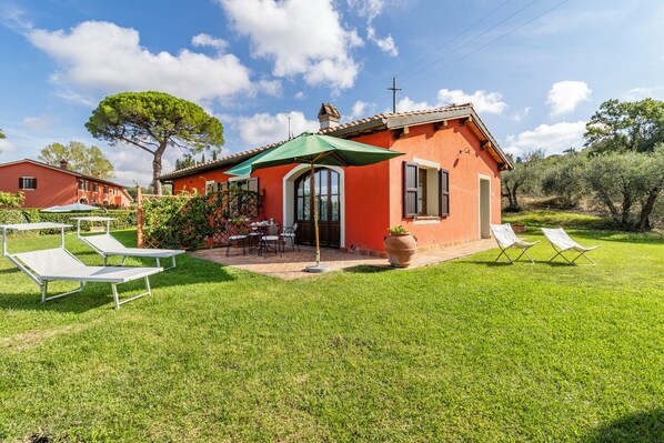 A red villa with a patio, outdoor seating, and a large tree.