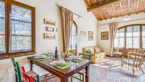A dining area with a wooden table set for four, surrounded by green and red chairs. There is a sofa and a wicker chair in the background. - Agriturismo Maramaldo (Castelfiorentino)