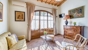 A cozy room with a wooden ceiling, a sofa, a table with a potted plant, a chair, a dresser, and a painting on the wall. - Agriturismo Maramaldo (Castelfiorentino)