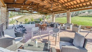 An outdoor patio with wicker furniture, a brick table, and a pergola structure. - Agriturismo Maramaldo (Castelfiorentino)
