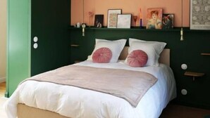 Une chambre à coucher avec un lit, des murs verts, un luminaire au plafond et des tableaux encadrés accrochés au mur.
