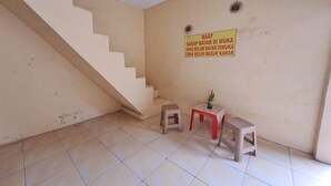 A room with a staircase, two stools, and a small table with a plant. A sign on the wall reads "MAAF HARAP BAYAR DI MUKA YANG BELUM BAYAR DI MUKA TIDAK BOLEH MASUK KAMAR." - Hotel O Venus Homestay Syariah Near Universitas Megou Pak Tulang Bawang (Menggala)