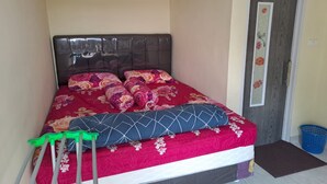 A neatly made bed with floral bedding, a dark headboard, and a blue laundry basket beside a door with a floral design. - Hotel O Venus Homestay Syariah Near Universitas Megou Pak Tulang Bawang (Menggala)