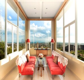 Ein geräumiger Raum mit zwei roten Sofas, einem Couchtisch und Blick auf eine Stadtkulisse durch große Fenster.