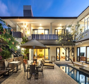Ein modernes Haus mit Pool, Sitzgelegenheiten im Freien und einer Treppe zu einem Balkon.